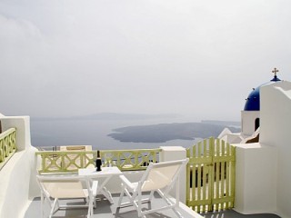 A white Santorini balcony next to a tiny chapel, with views across the bay