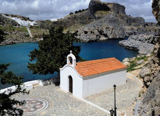 Agios Pavlos Chapel on the bay of the same name, with Lindos white village and rocky acropolis ruins behind, Rhodes